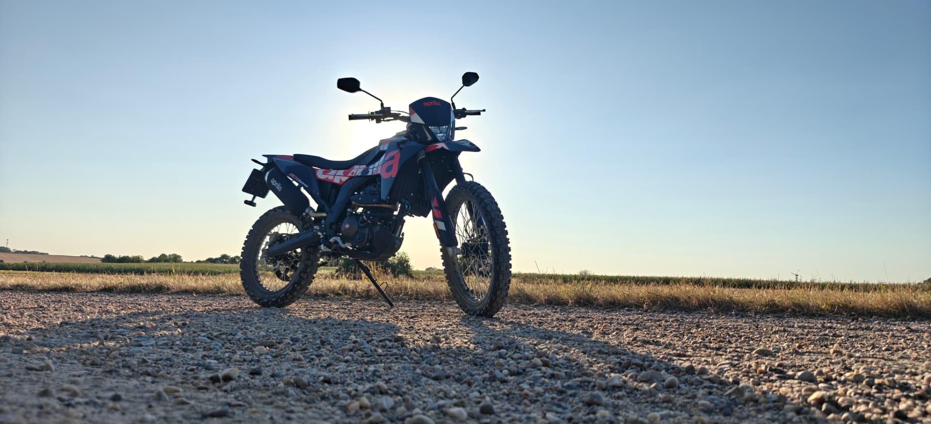 Motocykl Aprilia RX 125 na żwirowej drodze o zachodzie słońca